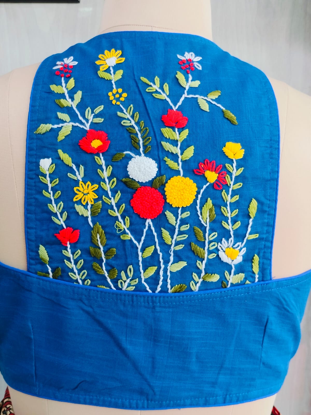 Close-up of red yellow and white floral hand embroidery on blue cotton